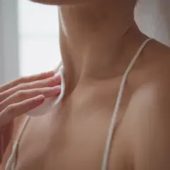 A hand holds a cotton pad to a person's neck and shoulder area.