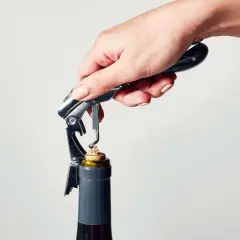 En hand använder en korkskruv för att öppna en vinflaska. Korkskruven har en metallspiral som liknar korkskruvar hår.
