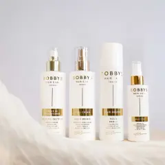 Fyra vita flaskor med guldfärgade detaljer från Bobby's Hair Care. En huskur mot statiskt hår.
