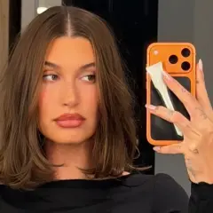 En kvinna med fina hårfrisyrer tar en selfie med sin orangea mobil.