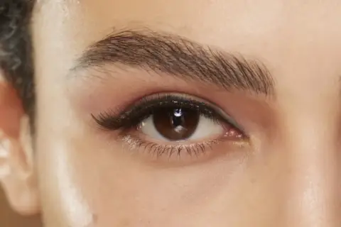 Närbild på ett brunt öga med perfekt trådade ögonbryn, dramatisk eyeliner och voluminösa fransar.