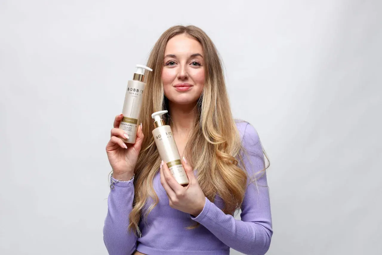 En kvinna med långt, blont hår håller upp två flaskor från Bobb's Hair Care. Hon har tunt hår och hoppas på att dessa produkter ska hjälpa.