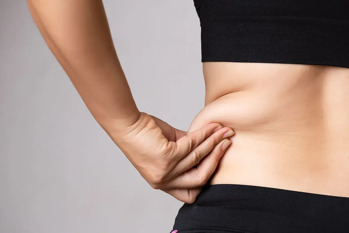 En hand som klämmer på fett på sidan av midjan, en vanlig indikation för coolsculpting.