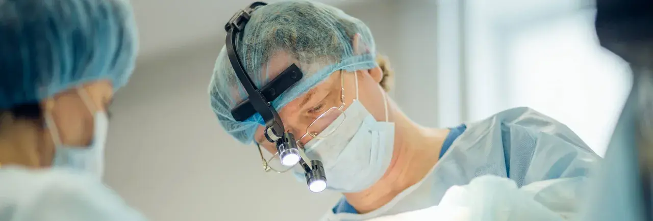 Kirurg med lupp och mask utför buccal fat removal i Sverige.