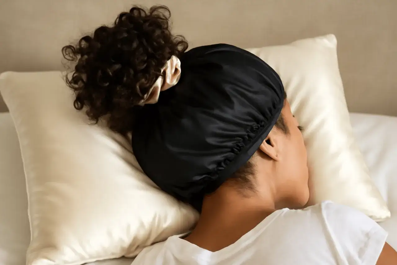 En person sover med en svart satinmössa för att skydda håret. En skön sömn med inpackning är en lyx.