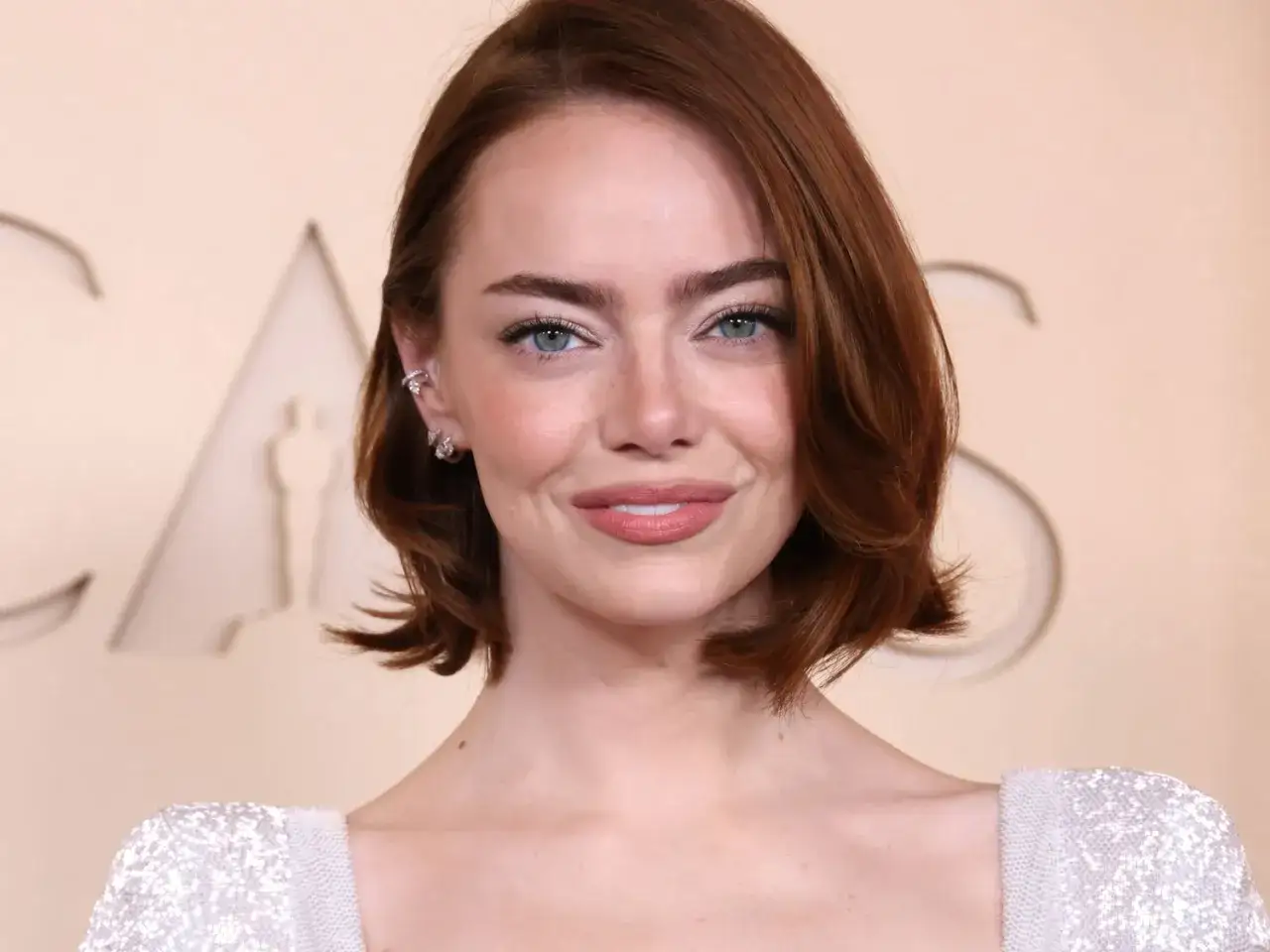 Emma Stone med korta frisyrer tunt hår, blå ögon och glittrig klänning.